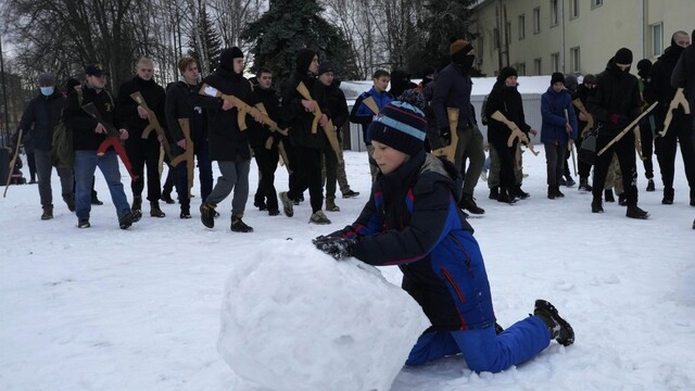 Chlapec vytvára snehovú guľu a  miestni obyvatelia sa účastnia na vojenskom výcviku v Kyjeve v nedeľu 30. januára 2022.
