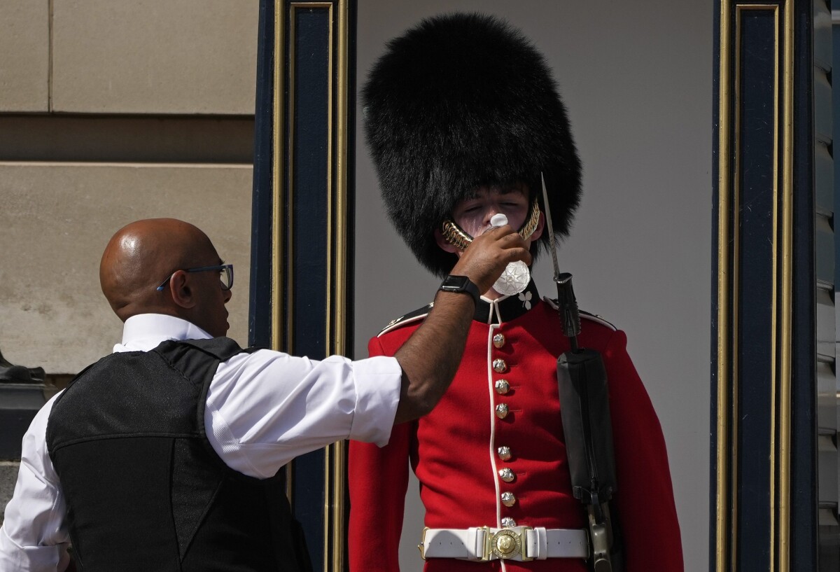 Policajt podáva vodu britskému vojakovi v tradičnom klobúku z medvedej kože, ktorý stojí spotený počas strážnej služby pred Buckinghamským palácom.