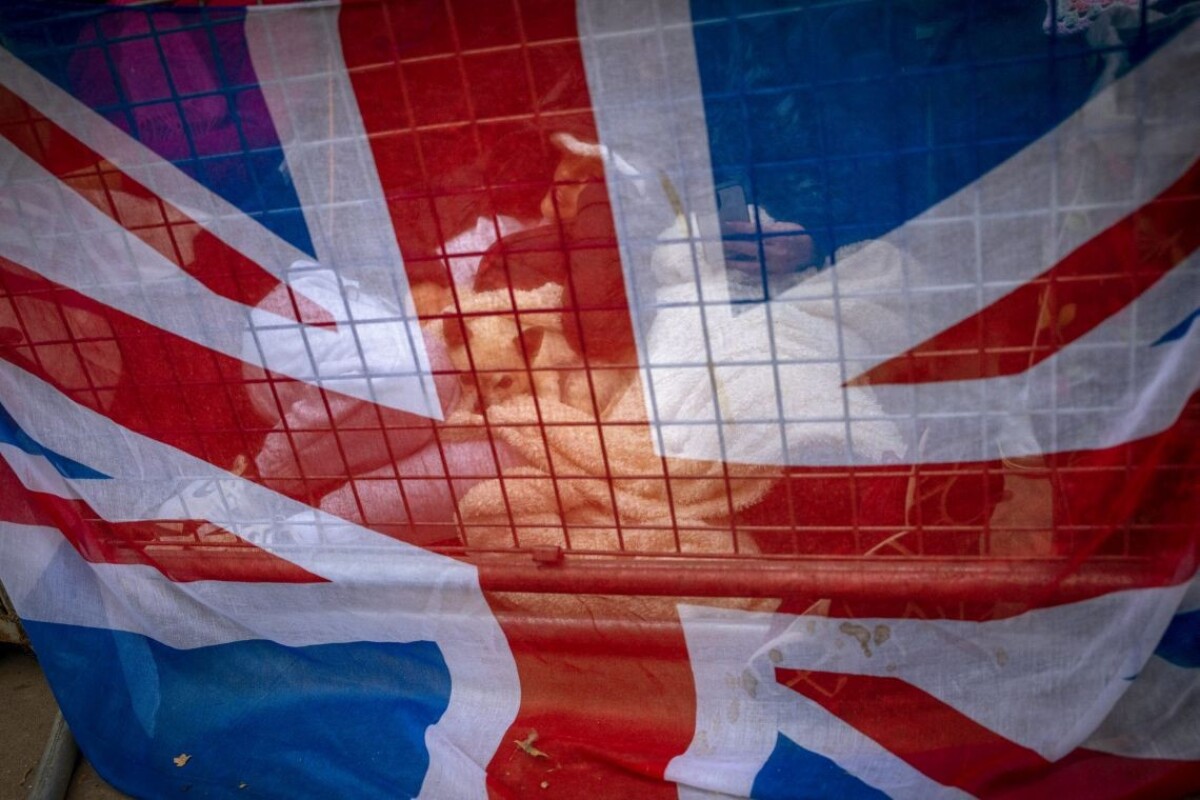 Smútiaci, vyobrazení cez vlajku Union Jack, čakajú pozdĺž cesty, na ktorej bude rakva kráľovnej Alžbety II