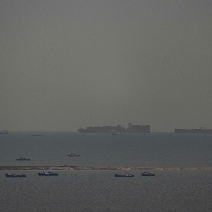 Rybárske člny na mori a nákladné lode v pozadí plávajúce cez Arabský záliv smerom k Hormuzskému prielivu pri Spojených arabských emirátoch v piatok 27. marca 2026.